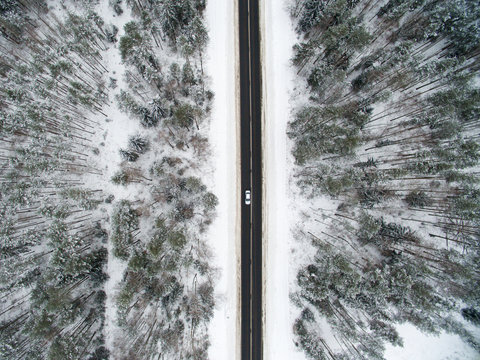 Winter forest and asphalt road. View from above. The photo was taken with a drone. Pine and spruce forest with a black road in the snow