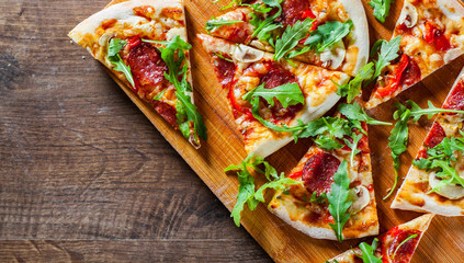 slices Pizza with Mozzarella cheese, mushrooms, pepperoni, tomato sauce, salami, pepper, Spices and Fresh arugula. Italian pizza on wooden table background