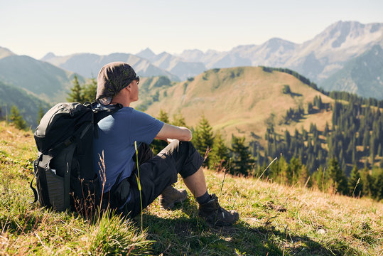 Mann sitzt mit Rucksack auf einem Berg und schaut die Bergkulisse an
