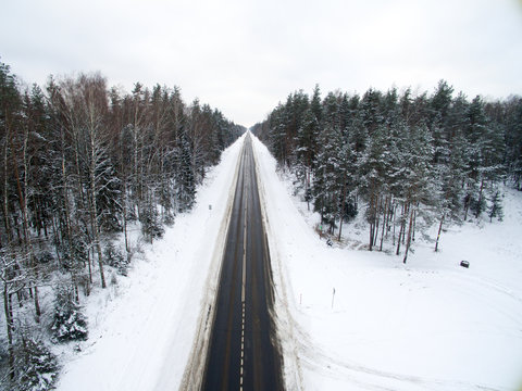 Winter Forest And Asphalt Road. View From Above. The Photo Was Taken With A Drone. Pine And Spruce Forest With A Black Road In The Snow