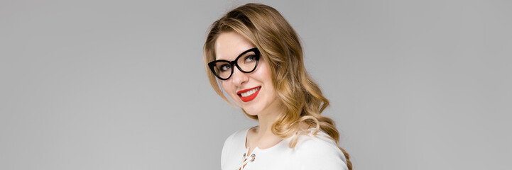 Fototapeta premium Attractive young blonde business woman in black and white clothes smiling holding clipboard standing in office on gray background
