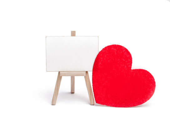 A red heart stands next to a canvas for text on a white isolated background. Concept of love and romance. Valentine's Day. Copy space