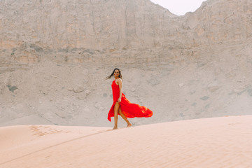 Young beautiful indian woman walking in red dress in the desert with mountains