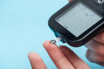 partial view of female fingers testing glucose level with glucometer isolated on blue background