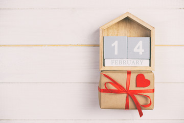 Cube calendar with red heart and gift box on wooden toned, vintage table with copy space. 14 February concept