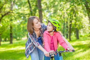 mother and daughter learning to ride a bicycle in summer park