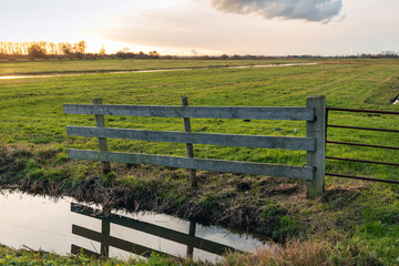 Wooden fence reflects in the mirror-smooth water surface of a polder ditch