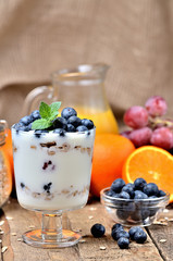 Yoghurt with oatmeal, fresh blueberries nad mint leaves and orange and grapes in background vertical photo