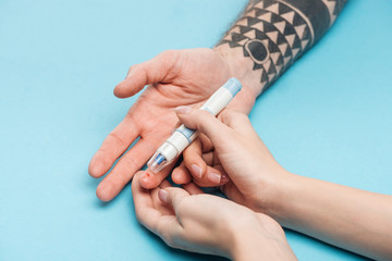 cropped view of woman testing man blood sugar level with syringe on blue background
