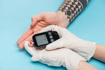cropped view of woman in gloves with glucometer on blue background