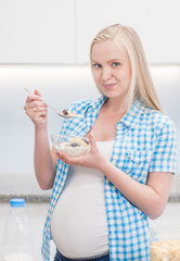 Smiling beautiful pregnant woman eating cereals at kitchen