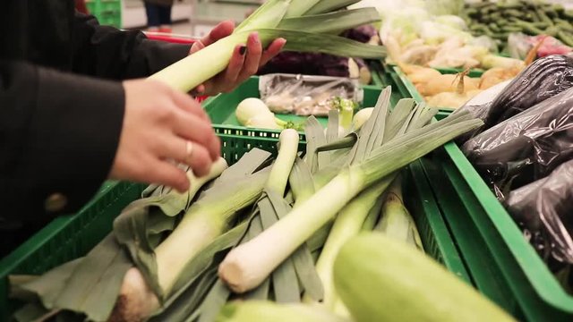 A woman's hand choosing and buying a lot of leek at a supermarket. Closeup shot.