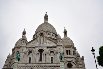 Basilica of the Sacred Heart (Sacre Coeur). Paris, France, Facade with statues, dome and towers. Rainy day, grey sky.