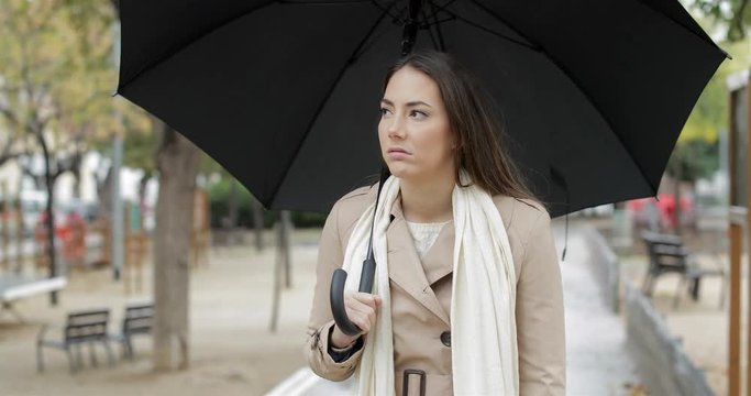 Front view portrait of a frustrated woman walking holding an umbrella complaining under the rain in winter