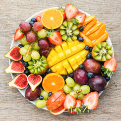 Fruits and berries platter, strawberries blueberries, mango orange, apple, grapes, kiwis on the grey wood background, copy space for text, square, top view, selective focus