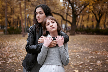 Portrait of pretty woman and teen girl. They are posing in autumn park. Beautiful landscape at fall season.