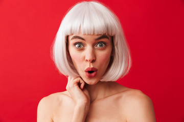 Excited young shocked woman dressed in carnival wig isolated over red wall background.