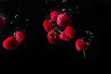 Raspberries falling in water  on a black background.