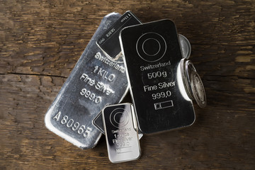 Silver bullion. Cast and minted bars and coins on a wooden texture background..