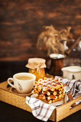 Breakfast with belgian waffles, jam and coffee on tray, rustic background