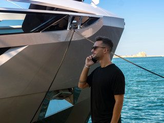 man is talking on a smartphone at the port  alongside a luxury boat
