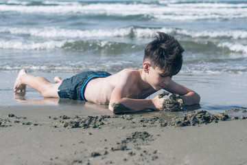 Happy teen boy having fun lying on the sand оn the beach at sunset