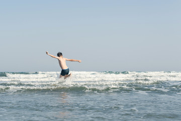 Fototapeta na wymiar Boy Jumping In Sea Waves with Water Splashes. Concept of summer vacation