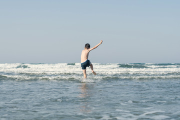 Boy Jumping In Sea Waves with Water Splashes. Concept of summer vacation