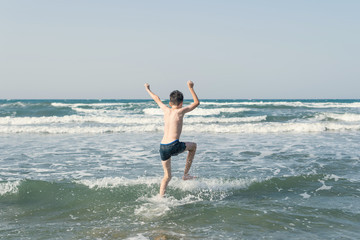 Boy Jumping In Sea Waves with Water Splashes. Concept of summer vacation