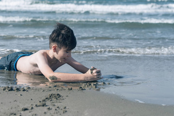 Fototapeta na wymiar Happy teen boy having fun lying on the sand оn the beach at sunset