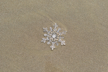 Huge sparkling snowflake on the sand in the sea foam. Concept of Winter and Christmas vacation on the beach and resort.