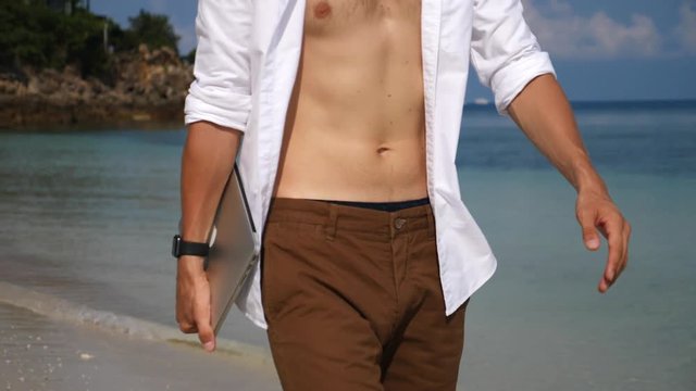 Young Sexy Man Holding Laptop And Walking On The Beach