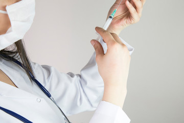 Hands in gloves filling medicine from ampule into syringe against the background of medical robe.