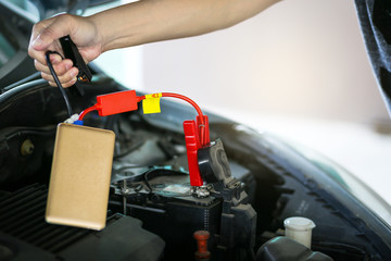 Close up of hand charging car battery with car power bank jumper starter.