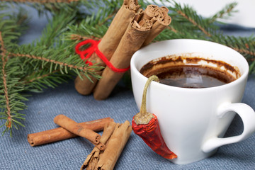Obraz na płótnie Canvas A cup of coffee on the table. Cinnamon sticks and pods of red pepper next to the fir branches. On a woven background.