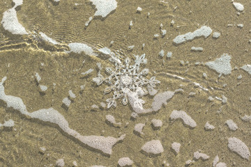 Huge sparkling snowflake on the sand in the sea foam. Concept of Winter and Christmas vacation on the beach and resort.