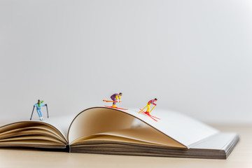 Miniature skiers sliding down the open book. Sport and travel concept