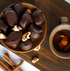 chocolates and walnuts in a plate on a wooden brown background