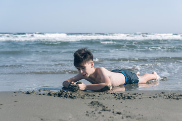 Happy teen boy having fun lying on the sand оn the beach at sunset