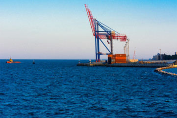 Odessa, Ukraine - August 8, 2018. Big working cranes for loading containerships and various cargoes to the ships at the shipyard against a beautiful evening blue sky in soft colors. Cargo delivery