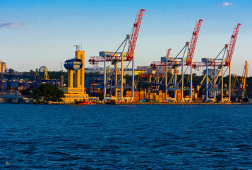 Odessa, Ukraine - August 8, 2018. Big working cranes for loading containerships and various cargoes to the ships at the shipyard against a beautiful evening blue sky in soft colors. Cargo delivery