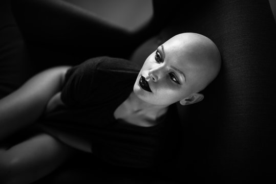 Emotive photo of a beautiful bald woman while sitting on a chair in a black tshirt.