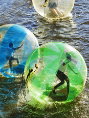 Few people in color water balls (similar to zorb or Human Hamster Ball) on river surface. Vltava river in Prague