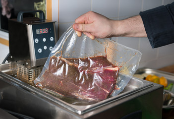 chef preparing food in kitchen. Packed beef meat is cooked for several hours in water at a temperature of 60 degrees, after which the meat is grilled