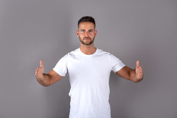 A handsome young man in a white tshirt showing something with his palms in front of a grey background in the studio.