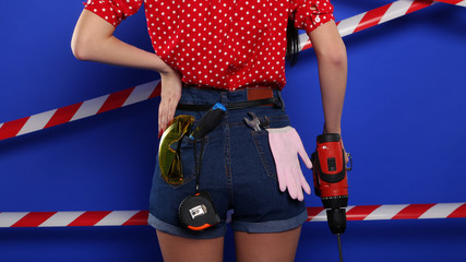 Short girl shorts in pockets which construction tools on blue background. Gloves, a screwdriver,...