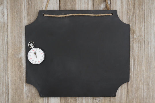 Hanging chalkboard with a stopwatch on weathered wood wall