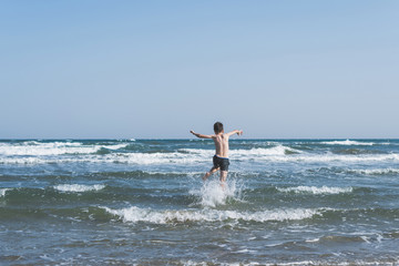 Boy Jumping In Sea Waves with Water Splashes. Concept of summer vacation