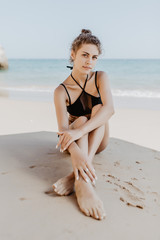 Fototapeta na wymiar Sexy fit woman in bikini sitting on beach on the ocean background