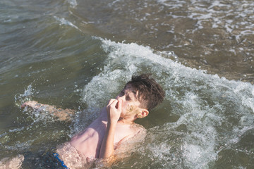 Teen boy closing his nose dives in the wave of sea in the tropical resorts. Concept of summer vacation